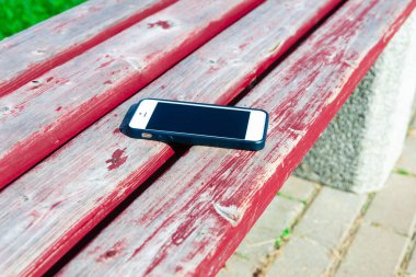 Parktaki bankta akıllı telefonu unutmuşsunuz. Bankta uzanan cep telefonunun yakın çekimi. Birisi cep telefonunu parkta bir bankta unutmuş..