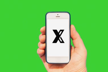 Ekranda X harfi olan cep telefonu tutan kişi. Parlak yeşil arka plan. Telsiai, Litvanya. 01-19-2023.