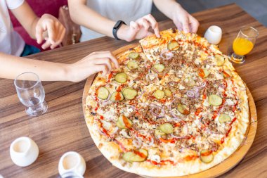 Pizzacıda bir araya gelen iki genç, lezzetli İtalyan yemeklerini paylaşırken eğleniyor, çeşitli meslekdaşlar ya da arkadaşlar pizza dilimlerini barda yiyor. Yaklaş, seçici odaklan..