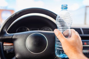 İnsan trafikte araba kullanırken elinde plastik su şişesi tutuyor. Yaklaş..