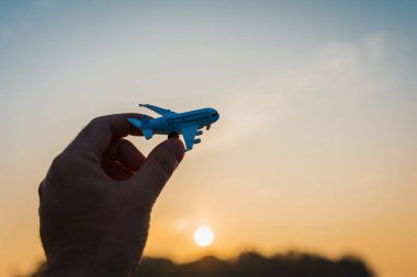 Bir adamın elindeki oyuncak uçak gökyüzünün arka planında bulutlu bir şekilde. Elinde uçak tutan ve bulutlu gün batımı üzerinde uçan adam mavi gökyüzü arka planı. Seyahat motivasyon konsepti..
