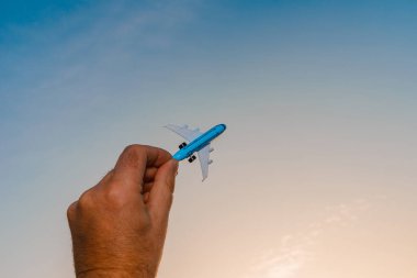 Bir adamın elindeki oyuncak uçak gökyüzünün arka planında bulutlu bir şekilde. Elinde uçak tutan ve bulutlu gün batımı üzerinde uçan adam mavi gökyüzü arka planı. Seyahat motivasyon konsepti..