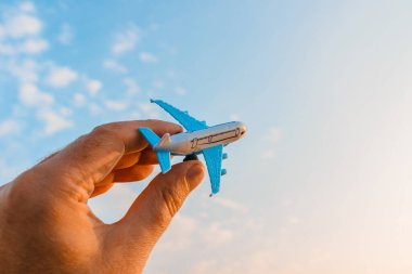 Bir adamın elindeki oyuncak uçak gökyüzünün arka planında bulutlu bir şekilde. Elinde uçak tutan ve bulutlu gün batımı üzerinde uçan adam mavi gökyüzü arka planı. Seyahat motivasyon konsepti..