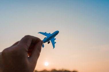 Bir adamın elindeki oyuncak uçak gökyüzünün arka planında bulutlu bir şekilde. Elinde uçak tutan ve bulutlu gün batımı üzerinde uçan adam mavi gökyüzü arka planı. Seyahat motivasyon konsepti..
