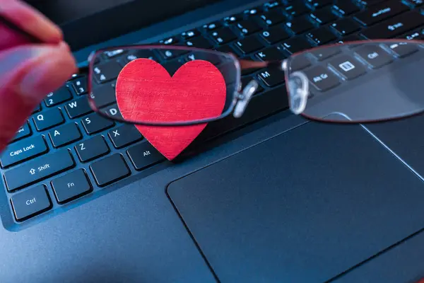 Remote senior date concept.distant video chat,red heart laptop keyboard with glasses.celebration, active leisure feeling alone.Close-up.