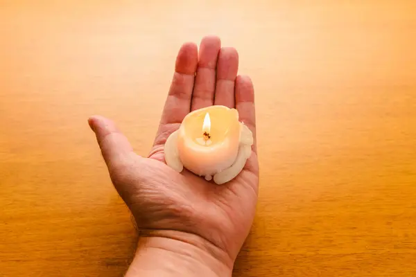 Man holding a lighted wax candle on a wooden background.Burning candle on the palm.Man holding a candle in the dark.
