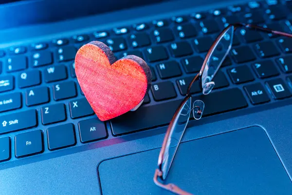 Remote senior date concept.distant video chat,red heart laptop keyboard with glasses.celebration, active leisure feeling alone.Close-up.