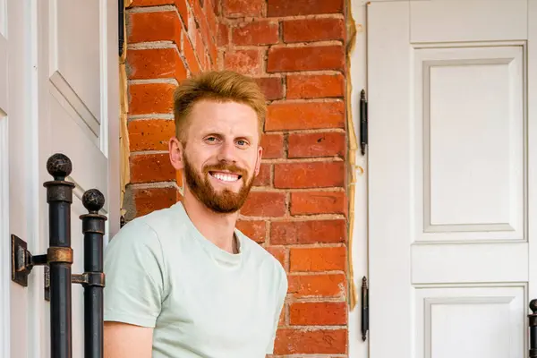 Portrait of Smiling Young Freckled Redhead bearded Man with red Facial Hair standing at old Brick Wall.Sunny summer day.Closeup.