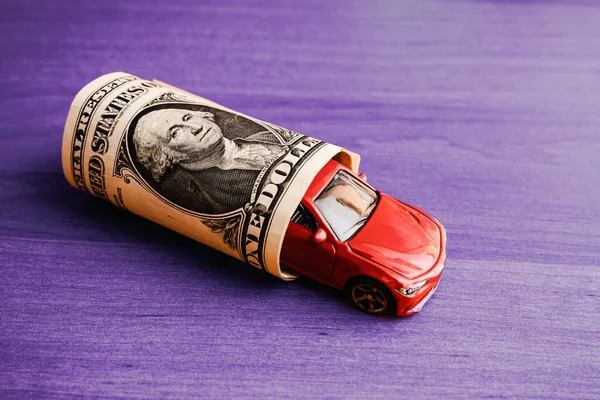 Concept of insurance, credit and car purchases,car loan.Auto dealership and rental, new car buy. toy car dollar bill on a purple table.