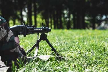 Bir asker makineli tüfekle ateş ediyor, bir asker çimlerin üzerinde yatıyor..