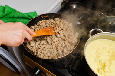 A housewife frying minced meat with onions in a frying pan. Frying Minced Meat. clipart