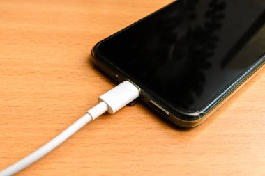 USB kablosu olan akıllı telefon masanın beyaz kablosunu şarj ediyor..