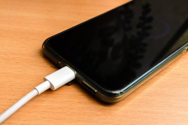 USB kablosu olan akıllı telefon masanın beyaz kablosunu şarj ediyor..