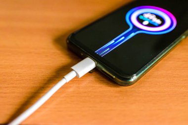 USB kablosu olan akıllı telefon masanın beyaz kablosunu şarj ediyor..