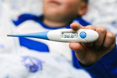 Çocukta yüksek sıcaklıkta elektronik termometre var. Çocuk yatakta yatıyor, yakın plan..