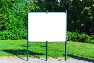 Yazın arka planında yeşil ağaçlar olan yeşil bir parkta beyaz ilan panosu boş..