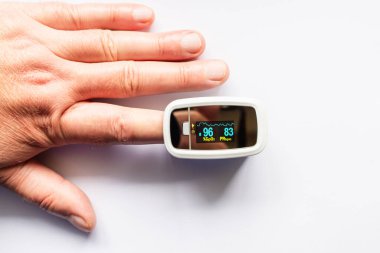 Beyaz arka plandaki kandaki oksijen seviyesini ölçmek için nabız oksimetresi kullanan bir adam test yapıyor..