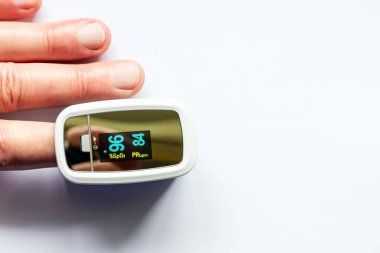 Beyaz arka plandaki kandaki oksijen seviyesini ölçmek için nabız oksimetresi kullanan bir adam test yapıyor. Boşluğu kopyala.