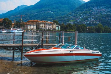 Lugano Gölü kıyılarına demirlemiş modern tekne ve uzaktaki yemyeşil yemyeşil İsviçre Alpleri, Lugano, İsviçre.