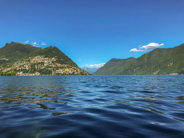 stock image Stunning landscape of picturesque Lake Lugano and the green lush Swiss Alps in the distance. Idyllic town Lugano, Switzerland, on a sunny summer day.