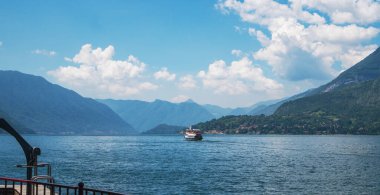 Güneşli bir yaz gününde arka planda yeşil İsviçre Alpleri ile Como Gölü boyunca giden feribotun güzel panoramik manzarası. Lombardy, İtalya.