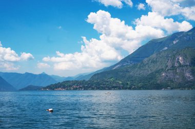Güneşli bir yaz gününde arka planda yeşil İsviçre Alpleri ile Lugano Gölü boyunca seyreden sürat teknesinin güzel panoramik manzarası. Ticino Kantonu, İsviçre.