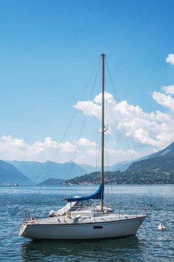 Varenna, Lombardy, İtalya kıyıları yakınlarındaki beyaz tekneyle güneşli bir yaz gününde, arkasında yeşil dağlarla Como Gölü 'nün büyüleyici manzarası..