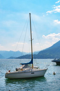 Şık beyaz yelkenli İtalya 'daki Varenna kıyılarına demir attı. Bir yaz günü arka planda Como Gölü ve Alpler 'in güzel İtalyan manzarası.