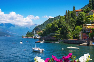 Lombardy, İtalya 'nın büyüleyici bir ortaçağ köyü olan Varenna kıyısı yakınlarındaki balıkçı tekneleriyle Como Gölü' nün büyüleyici manzarası. Güneşli bir yaz günü, arka planda yeşil İsviçre dağları ile birlikte..