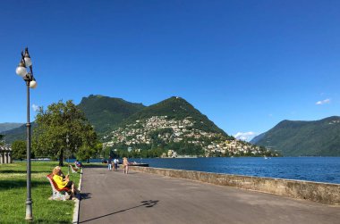 İsviçre 'deki Lugano Gölü kıyısındaki Paradiso' daki Lakeshore Gezinti Alanı boyunca yürüyen insanlar..