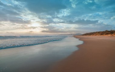 Fırtınadan önce gün batımında kıyıya vuran el değmemiş bir sahil ve okyanus dalgalarının geniş panoramik görüntüsü. Avustralya 'nın Güneş Işığı Sahili' nde çarpıcı bulutlar ve deniz manzarası.