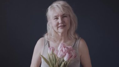 Geçmişinde çiçekler olan olgun, beyaz bir kadın. Stüdyoda pembe laleli yetişkin bir bayan..