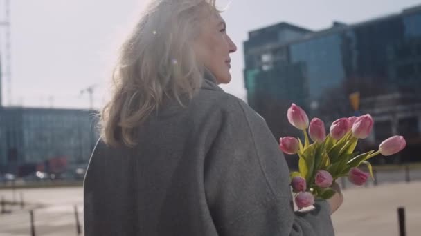 一位高个子白人优雅的女人手握一束粉红色的郁金香沿街走着 阳光灿烂的春天 女性的概念 — 图库视频影像