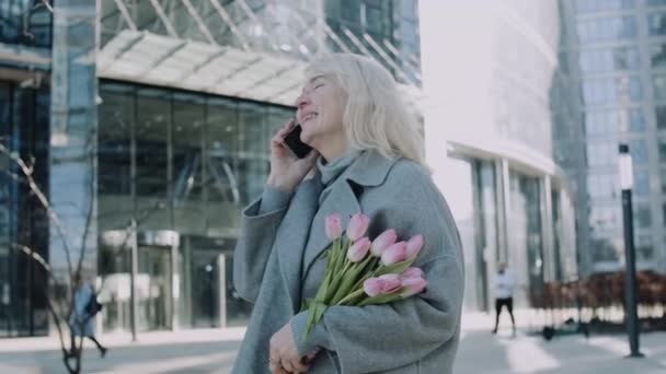 Starsza Elegancka Kobieta Rozmawia Przez Telefon Trzymając Bukiet Różowych Tulipanów — Wideo stockowe