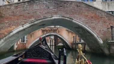 Venedik 'teki küçük köprülerin altında gondolda bir gezinti. Turistler kanal boyunca geleneksel taşımacılıktan hoşlanıyorlar.