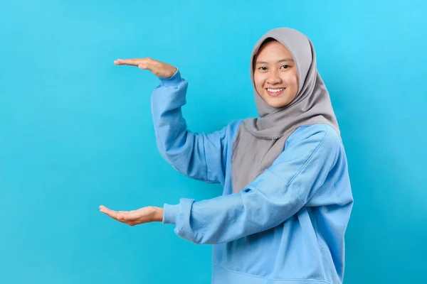 身穿蓝色毛衣的快乐而美丽的亚洲女人 在蓝色背景的手掌之间展示了一个复制的空间 — 图库照片