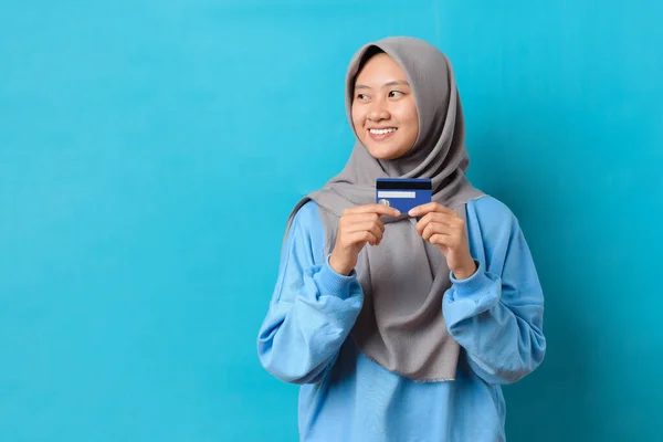 明るい幸せな若いインドネシアの女性のイメージコピースペースを見て デビットカードまたはクレジットカードを保持する笑顔青の色の背景に隔離された店を購入 — ストック写真