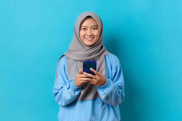 幸せを感じるインドネシアの女性の肖像と青い背景にスマートフォンを持つカメラを見て 可愛いですインドネシアの女の子笑顔身に着けているカジュアルヒジャーブと接続インターネットショッピングオンライン — ストック写真