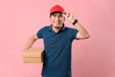 Kırmızı şapkalı mutlu teslimatçı elinde bir posta kutusuyla pembe arka planda duruyor..