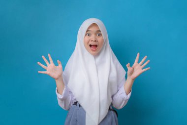 Emotional portrait of scared high school girl looking surprised with fear in her eyes isolated on blue background. People and human expressions and emotions concept