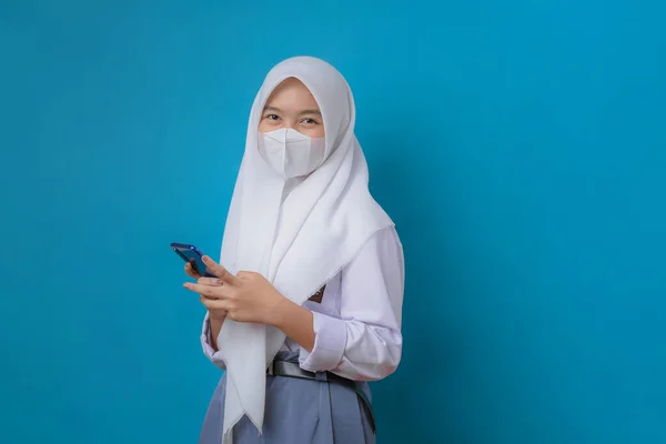 女学生使用带制服的手机 戴口罩 拍摄工作室 蓝色背景隔离 — 图库照片