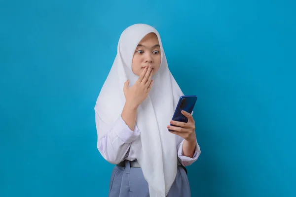 Surprised High School Girl Looking Smartphone While Standing Blue Background — стоковое фото