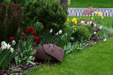 Kharkov, Ukraine, 14 May 2024. A garden decorated with metallic hedgehog sculptures. There are flowers of different colors, including red and yellow tulips and white daffodils. The surrounding grasses and shrubs are well tended, and a small paved pat clipart