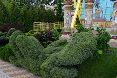 Kharkov, Ukrayna, 14 Mayıs 2024. Manikürlü yeşilliğin soyut ot formlarına dönüştüğü bir bahçe sahnesi. Arka planda, Mısır tarzı duvar resimleri ve dekorasyonlarla süslenmiş sütunlar var. Dekor yeşillik, fayanslı asfalt ve 