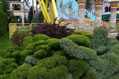 Kharkov, Ukrayna, 14 Mayıs 2024. Arka planda süslü çalıları ve ağaçları olan iyi korunmuş bir bahçe. Sarı ve kırmızı tonlarda tuğla bir yol ve arka planda mimari olarak tasarlanmış bir yapı vardır. Işık direği de görünür.