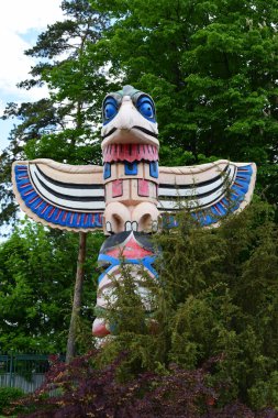 Kharkov, Ukraine, 14 May 2024. A large bird-shaped totem with bright colors, such as red, blue and white. It is located in a green environment, surrounded by trees and bushes under a partly cloudy sky. clipart