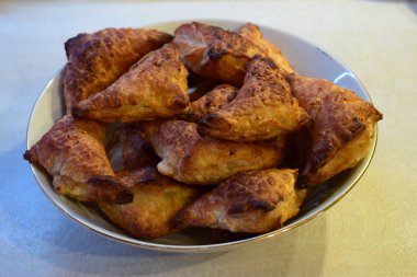 Bir kase dolusu üçgen, altın-kahverengi hamur işi. Hamur işleri yumuşak bir dokuya sahip iyi pişmiş gibi görünüyor, muhtemelen puf böreğinden yapılmışlar.