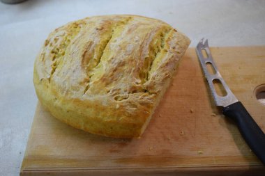 Bir somun taze pişmiş ekmek, altın kahverengi, çıtır çıtır bir kabuk ve yumuşak, kabarık bir iç döşeme, yanında bir ekmek bıçağı ile ahşap bir kesme tahtası üzerinde dilimlenmiş