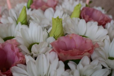 Bir buket çiçeğin manzarası. Birincil çiçekler sarı yeşil merkezli beyaz papatyalardır. Papatyaların arasında açık pembe çiçekler, lisianthus ve bazı tomurcuklar bulunur.