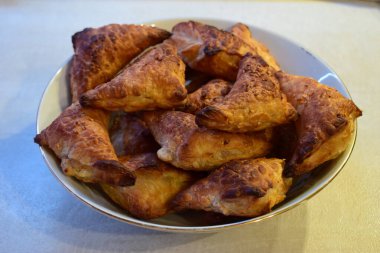 Bir kase dolusu üçgen, altın-kahverengi hamur işi. Hamur işleri yumuşak bir dokuya sahip iyi pişmiş gibi görünüyor, muhtemelen puf böreğinden yapılmışlar.